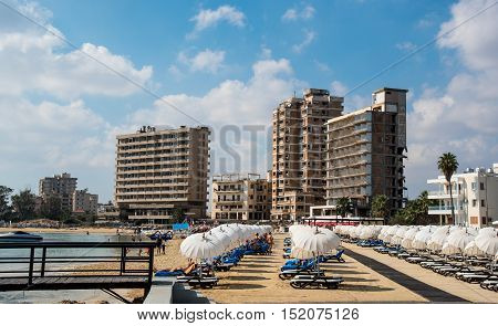 Famagusta Cyprus - September 15 2016: Palm Beach with beach umbrellas and tourists and the abandoned hotels at Varosha ghost town Famagusta Northern Cyprus