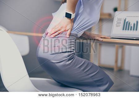 Working hard. Beautiful young woman rising from a chair and touching back while having backache.