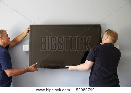 Two Men Fitting Flat Screen Television To Wall