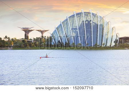 Singapore, Republic of Singapore - May 4, 2016: Woman on kayak crossing Marina Bay at sunset. Supertree grove and Cloud garden on background