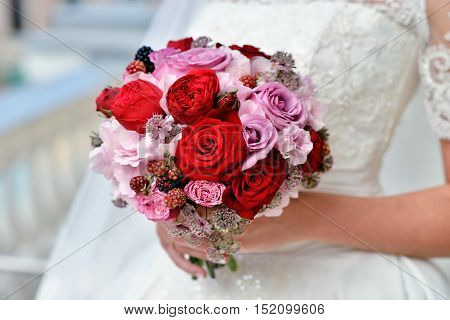 Beautiful bride is holding a wedding colorful bouquet. Beauty of colored flowers. Close-up bunch of florets. Bridal accessories. Female decoration for girl. Details for marriage and for married couple