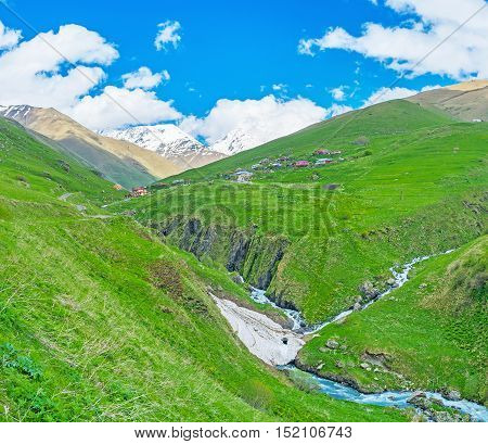 The picturesque Juta village on the juicy green slopes located by the fast flowing Jutistskali river covered with snowfields Georgia.