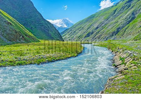 The Snostskali river runs along the narrow Sno gorge with the snowy peak of Kazbek Mount on the background Kazbegi Georgia.