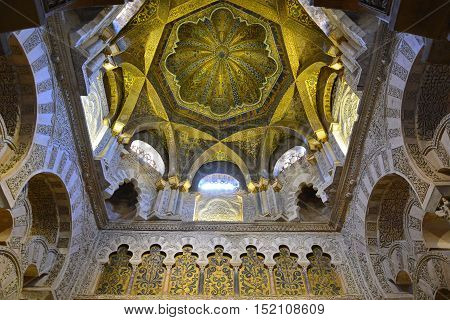 Cordoba, Spain - July 18, 2015. Ornate ceiling above the mihrab in the Mezquita of Cordoba, with paintings and inscriptions. The entire mihrab portal incorporates 1600kg of gold mosaic cubes, a gift from the Christian emperor of Byzantium.