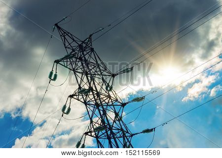 A high voltage power pylons against blue sky. The photo shows a blue sky with cloud through which the sun shines