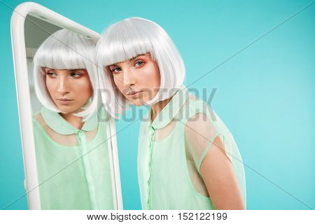 Portrait of stylish young woman in blonde wig near the mirrror