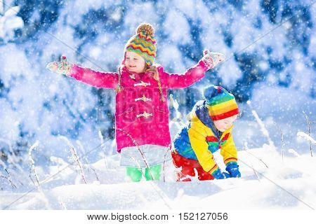 Child running in snowy forest. Toddler kid playing outdoors. Kids play in snow. Christmas vacation in sunny winter park for family with young children. Little girl in colorful jacket and knitted hat.