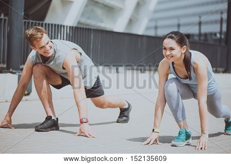 Couple exercising together. Beautiful young woman and a handsome athletic man smiling and preparing for a run outdoors while standing in sprint start position.