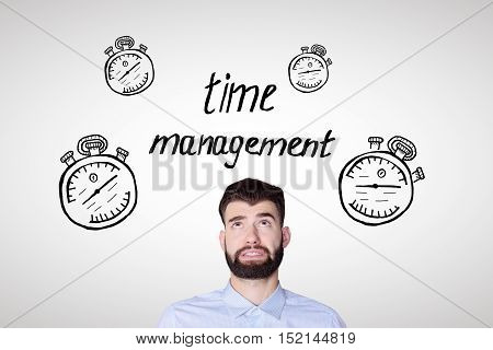 Portrait of worried young man on light background with creative clock skethes. Time management and deadline concept