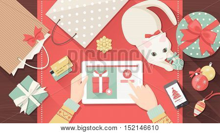Woman purchasing Christmas gifts online using a tablet her cat is playing with a bauble on the desk holiday and celebrations banner