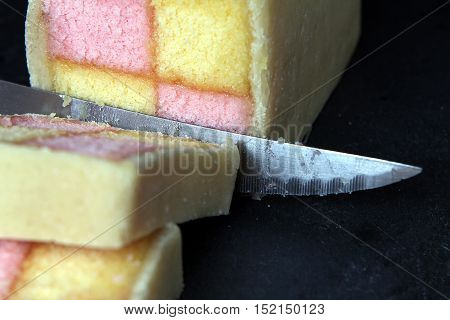 Freshly Cut Battenberg Cake On Dark Slate Background With Knife. Pink And Yellow Sponge Covered In M