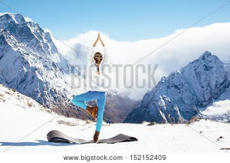 Young woman practicing yoga pose outdoors in winter. Stretching workout in snow on top of mountain. Hiking in cold season. Calm and silent view.