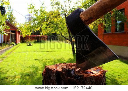 Axe on a stump in a garden with a lawn mower and a red house wall at the background