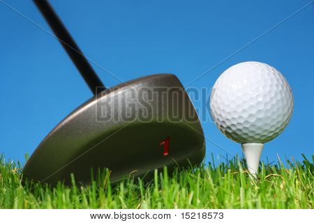 Klaar om te rijden een golfbal uit een tee met gras en een blauwe achtergrond.