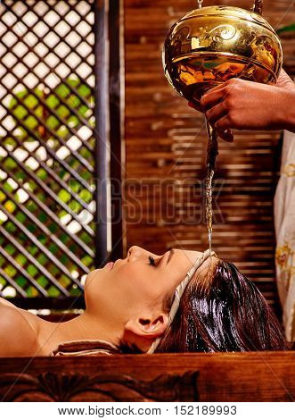 Young woman having pouring oil massage in India spa treatment. Shirodhara Pouring oil on head. Green plants outside.