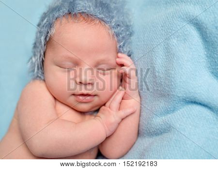 sweet newborn baby with smile sleeping on hand with blue hat on his head