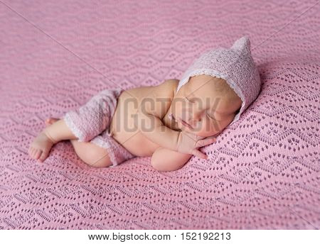 lovely sleeping newborn baby in pink hat and panties on pink blanket