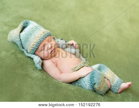 lovely newborn baby in knitted hat and panties sleeps curled up, top view