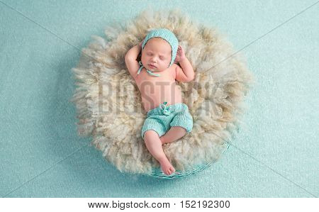 funny newborn boy sleeping with hands behind his head on round fluffy bed