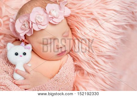 lovely sleeping newborn girl holding toy on pink fluffy blanket