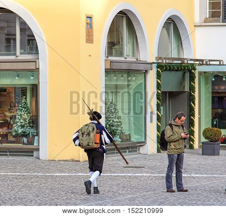 Zurich, Switzerland - 11 December, 2015: scene on the Munsterhof square in the old town of the city: a person in medieval clothing carrying a halberd, a person with a mobile phone, windows of a store with Christmas decorations.