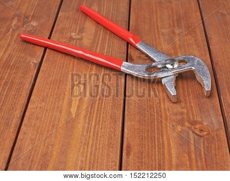 Metal plumber wrench with red handles on wooden brown surface