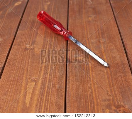 Cruciform screwdriver with the red handle on wooden brown surface