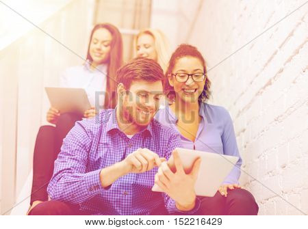 business, technology and startup concept - smiling creative team with tablet pc computer sitting on staircase