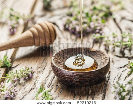 Herbal honey pouring into the wooden bowl. Bowl is on old wooden table surrounded with levender flowers.