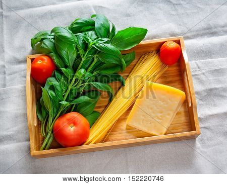 Green basil chunk of parmesan cheese raw cappellini and tomatoes on wooden tray