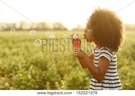 Little African American girl blowing bubbles in field