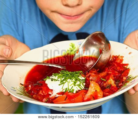 Ucrainian russian traditional vegetarian red soup - borsch in blue plates on wooden background. Top view with soup ladle sore cream and parsley with kids hands and mouth