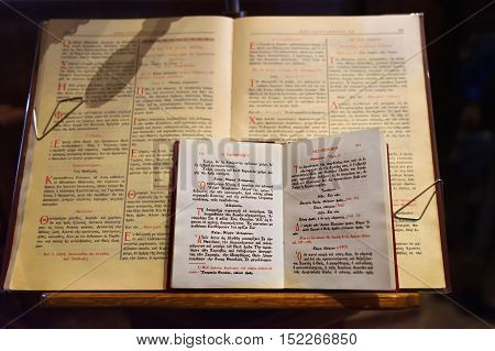 Meteora, Greece - Sept 27, 2016: The pulpits or the byzantine ambos in christian orthodox church where scriptures to read. In the foreground the open ancient holy Bible and prayer books in the greek language illuminated by dim of candles light. Greece