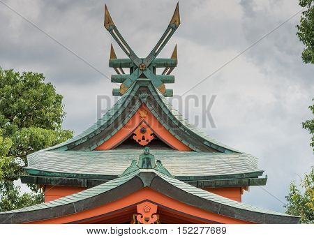 Kyoto Japan - September 17 2016: Windmill like roof structure at Fushimi Inari Taisha Shinto Shrine. Green tiles red facial boards cloudy sky fixed gold tipped wings.