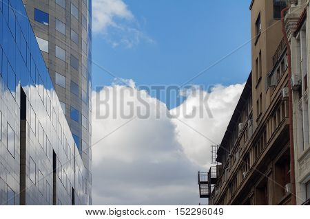 Side by side photo of classical building in front of modern glass office building with blue sky in between