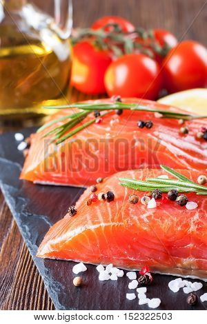 Raw salmon fillet and ingredients for cooking on a slade board and brown wooden background.