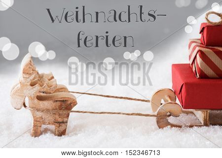 Moose Is Drawing A Sled With Red Gifts Or Presents In Snow. Christmas Card For Seasons Greetings. Silver Background With Bokeh Effect. German Text Weihnachtsferien Means Christmas Break