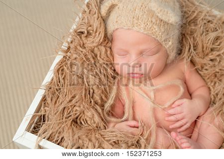 lovely newborn baby in knitted hat sleeping in wooden box with fluffy blanket