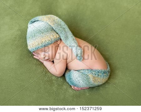 lovely newborn baby in knitted hat and panties sleeps curled up, top view