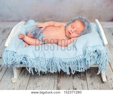 lovely newborn boy sleeping on little bed with blue diaper in hat and panties