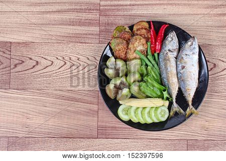 Ready side dish served  for Thai spicy sour dip   as deep fired mackarels,boiled long-eggplant,lentils,winged bean ,red hot chili pepper and sliced cucumber on wood.  Have text space on left.