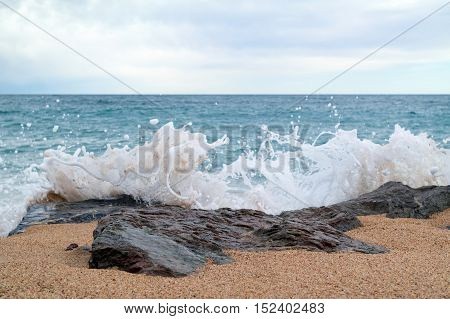 Lumpy sea at cloudy day. Seascape with rocky stones and splashes in the foreground