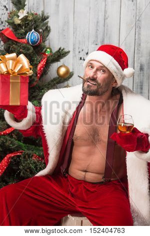 Portrait of sexy Bad Santa Clause congratulating everybody with New Yeat and Christmas holidays while posing for photographer in studio.