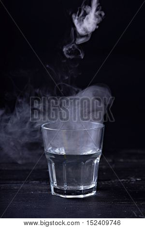 Hot water with a lot of steam in a glass at a black background. Dark photo