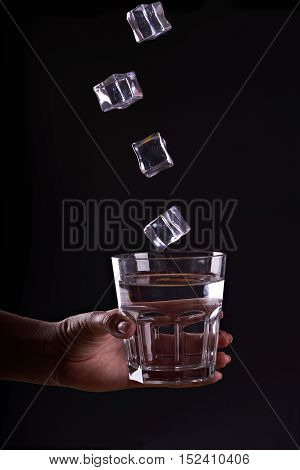 Woman holds a glass of water with ice cubes in motion . Give a glass of water. Drink more wate with icer. Black background.