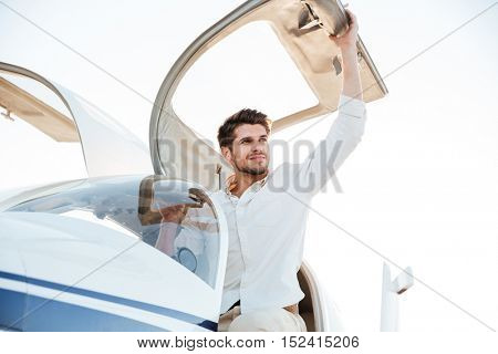 Cheerful young man pilot getting out of the plane after landing