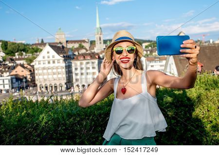 Young female tourist making selfie photo on the beautiful old townscape background in Zurich city. Having a happy vacation in Switzerland