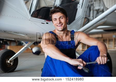 Happy smiling mechanic in overall resting after hard working day holding wrench