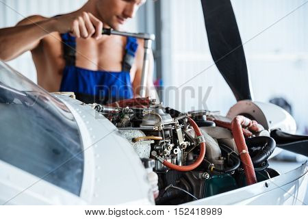 Cropped image of a repair man in overall fixing engine on a plane