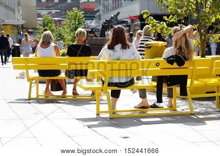 Stockholm, Sweden - August 4, 2015: Summer time at the street Sergel Arkaden in the city center off Stockholm with people sitting on yellow bench in the warm sun light.